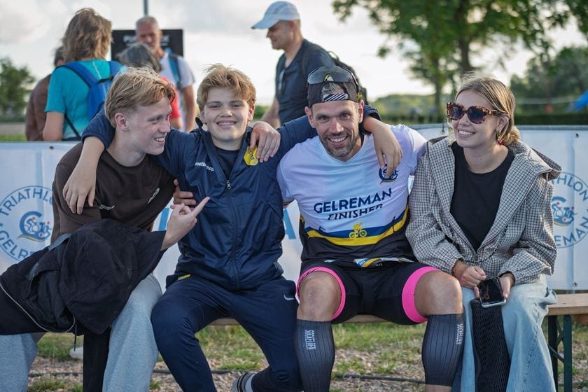 Finisher met medaille op een bankje tussen vrienden en familie