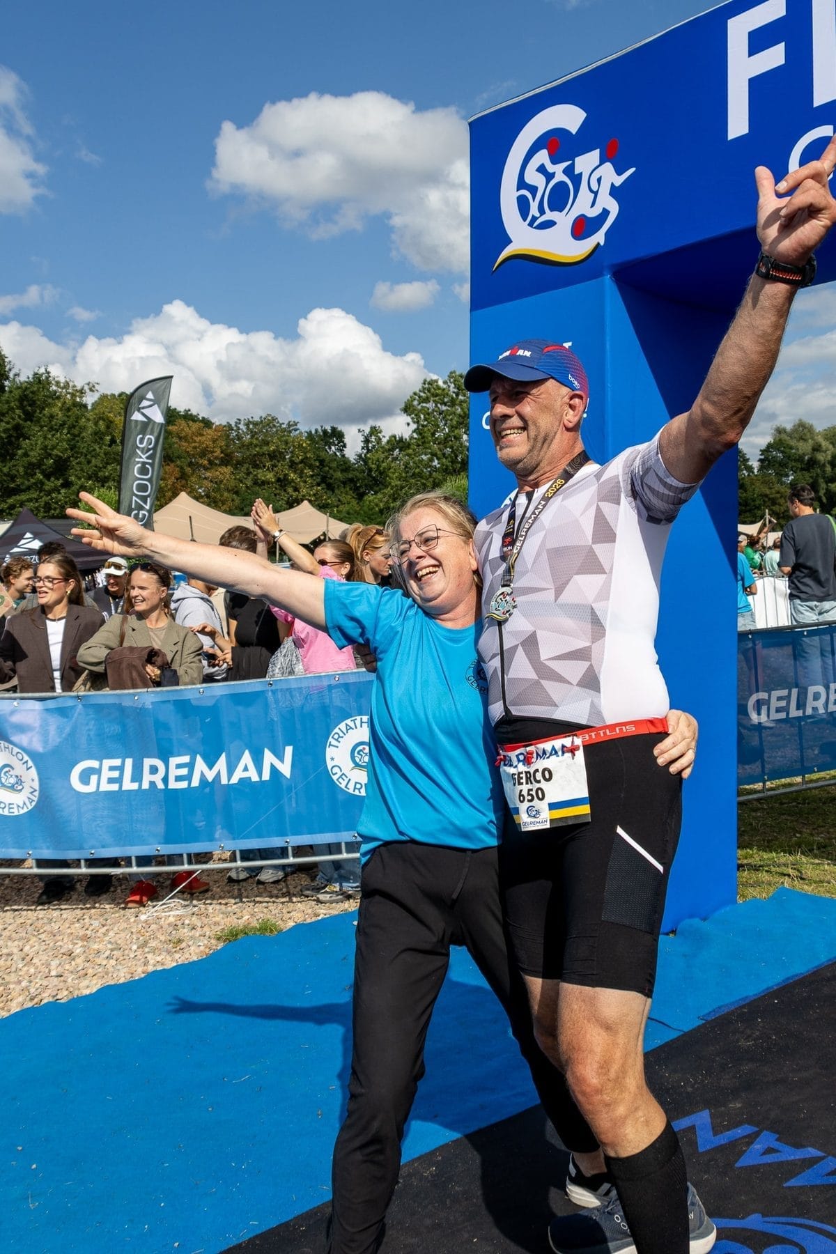 Vrijwilliger juicht met een finisher onder de finishboog